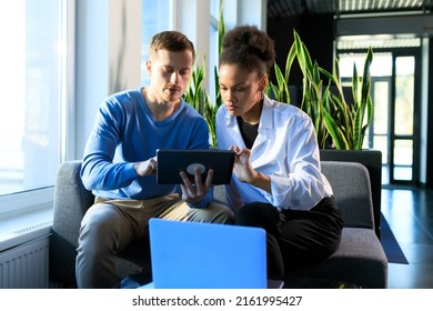 Two Colleagues Are Looking At The Tablet Screen While Sitting In The Office Lobby