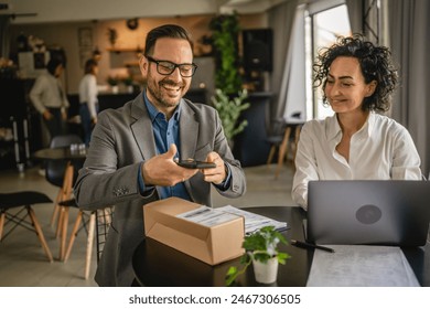 Two colleagues sit at cafe woman work on laptop check shipment drop shipping and man scan packets with mobile phone - Powered by Shutterstock