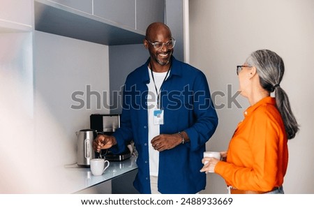 Two colleagues taking a coffee break, relaxing, having a conversation in a modern office kitchen.