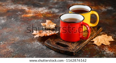 Two colored enamel tea cups, autumn maple leaves on rusty brown background