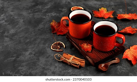 Two colored red and yellow enamel mugs with hot autumn drink, mulled wine with apples and cinnamon and autumn fallen leaves on a rusty table, seasonal banner or advertisement, hello autumn concept,