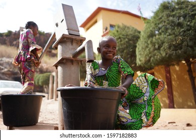 Two Colorful Dressed African Girls Fetching Water at the Borehole