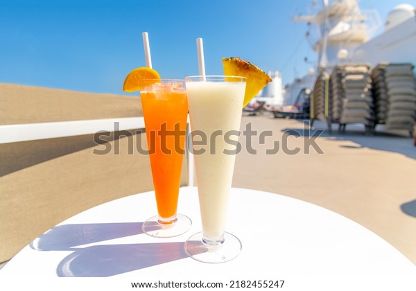 Two\
colorful mixed drinks with fresh fruit and a straw on the upper\
deck of a luxury cruise ship at sea on a sunny\
day.