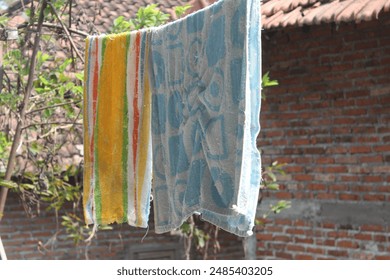 Two colorful towels drying on a clothesline against a brick wall backdrop. - Powered by Shutterstock