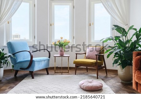 Two comfortable armchairs stand opposite each other, next to a coffee table with tulips in vase. Interior design in the style of the 60s. Old fashioned furniture in living room. Hygge apartment