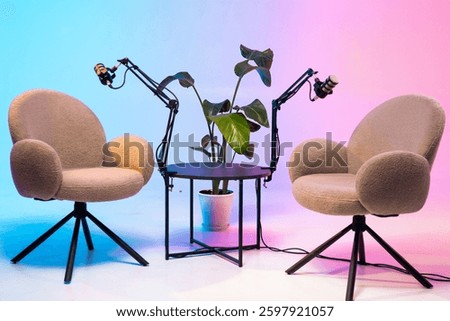 Two comfortable chairs create an inviting atmosphere for a podcast recording. Each chair is equipped with a microphone attached to flexible arms, surrounded by a vibrant backdrop and a plant.