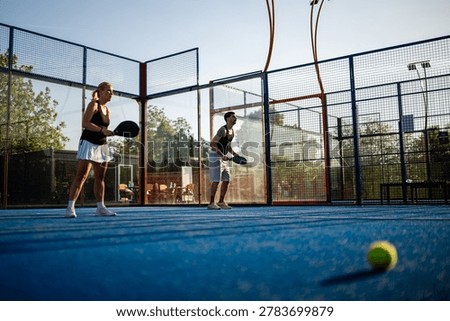 Two competitive athletes playing racket sport padel tennis on a blue outdoor court, a focus on active lifestyle