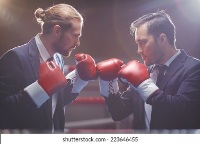 Two competitive businessmen in suits and boxing gloves attacking one another