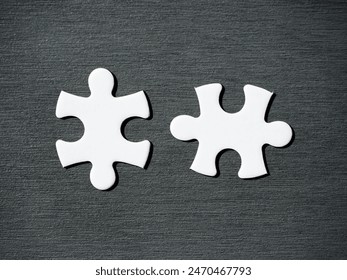 Two complementary white jigsaw puzzle pieces on a dark wooden table, symbol of association, connection or interdependence