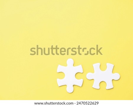 Two complementary white jigsaw puzzle pieces on a yellow background, symbolizing association, connection, or interdependence. Copy space to add text