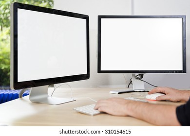 Two computer monitors with a white screen on a desk, with a man's hands on a keyboard in an office, suited for mock-ups and presentations, with plenty of copy space for your designs