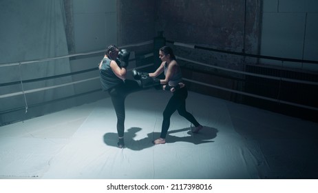 Two Confident Female Kickboxers Doing A  Sparring Session, Wearing Gloves As They Kick Each Other. Badass Women Fighters Training Together In An Old Boxing Gym Studio In A Boxing Ring.