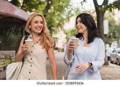 Two confident mature caucasian girlfriends women best friends sisters walking together and drinking hot beverage tea coffee in the morning outdoors in city park. - Shutterstock ID 2038993436