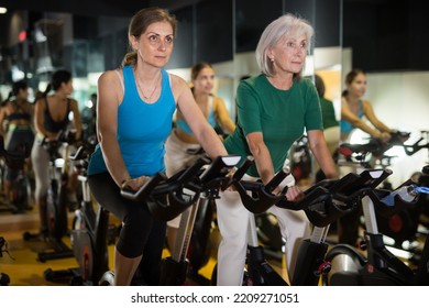 Two Confident Senior Women Warming Up On Bikes In Spin Class At Fitness Studio