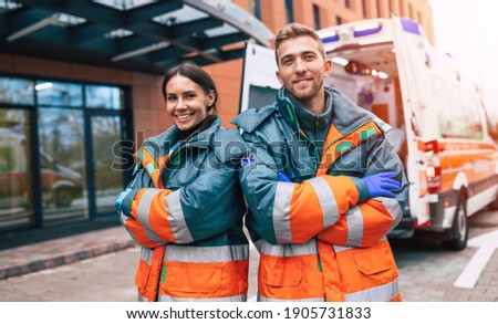 Two confident young doctors looking on the camera on ambulance and hospital background