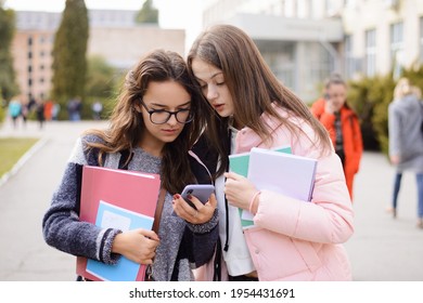 Two confused students reading bad news on the phone. Two shocked female students near the university building looking to the phone
