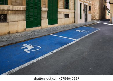 Two consecutive disabled parking spaces painted blue with white wheelchair symbols on a street next to green shutters.