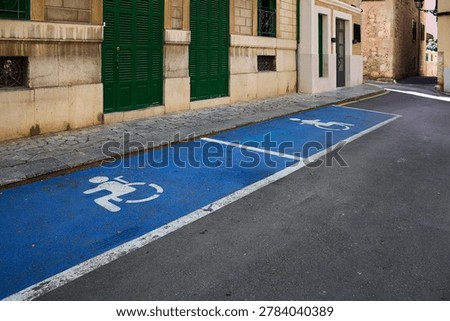 Two consecutive disabled parking spaces painted blue with white wheelchair symbols on a street next to green shutters.