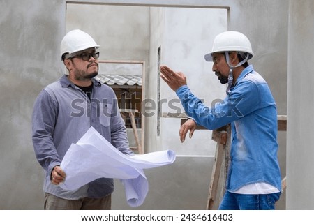 Two construction workers, architect, engineer, contractors clad in safety helmets and glasses, engage solving problem discussion and pointing roof or ceiling of the construction site, safety planning