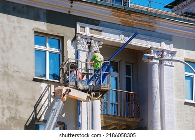 Two construction workers in bucket reconstructing facade of building, worker install plastering mesh before plastering and painting works. Workers restore facade in lifting  crane bucket. Facade work