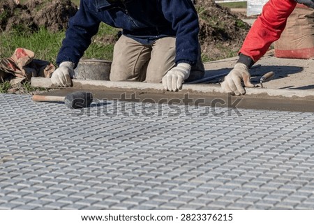 Two construction workers leveling mortar with a straight edge for paving tile installation