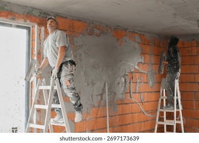 Two construction workers plastering and leveling the ceiling during interior renovation in a building with brick walls. Professional builders working on plaster application and wall finishing. 