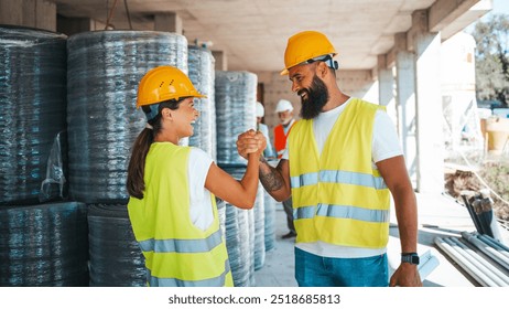 Two construction workers in safety gear exchange a confident handshake, symbolizing teamwork and success on-site. The atmosphere is positive and collaborative amidst industrial materials.