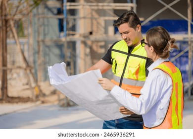 Two construction workers in safety vests reviewing a blueprint at an outdoor building site, collaborating and planning work. - Powered by Shutterstock