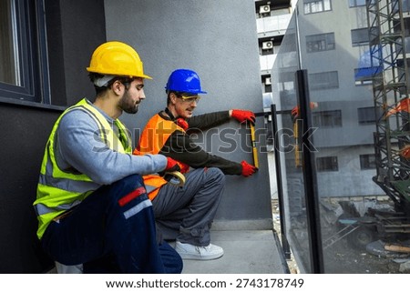 Two construction workers using spirit level to check wall alignment on a balcony.