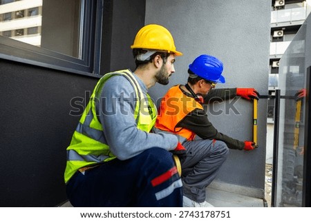Two construction workers using spirit level to check wall alignment on a balcony.