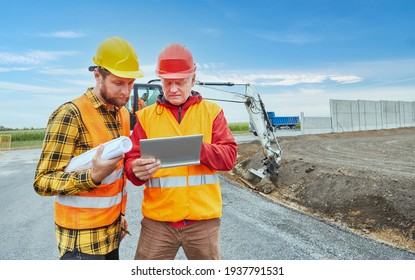 Two construction workers using tablet computer during road development on construction site