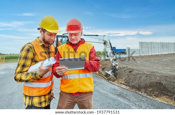 Two construction workers using\
tablet computer during road development on construction\
site