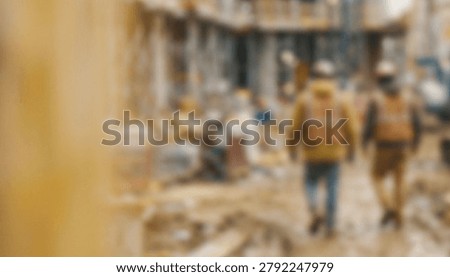 Two construction workers walk through a busy construction site, surrounded by machinery and building materials. The environment shows a blurred, active work zone.