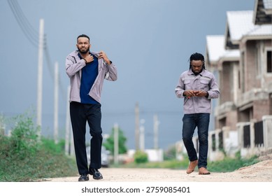 Two construction workers walking on road near housing construction site under dark storm clouds. Building industry workers commuting to jobsite, construction labor and urban development concept.