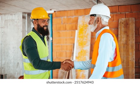 Two construction workers wearing safety gear shake hands at a building site, symbolizing teamwork and collaboration in the construction industry. - Powered by Shutterstock