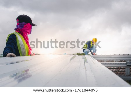 Two construction workers work on the steel roof structure of the building in the construction area. Use an electric drill to tighten the nut or install the roof of the house.