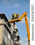 Two construction workers working on a lifting platform in an old part of a city, reconstruction of old buildings