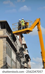 Two construction workers working on a lifting platform in an old part of a city, reconstruction of old buildings