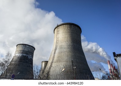 Two cooling towers emitting steam, with a blue sky background.