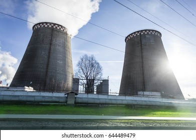 Two cooling towers emitting steam, with a blue sky background.