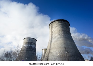 Two cooling towers emitting steam, with a blue sky background.