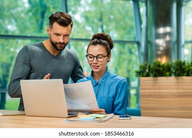 Two Cooperative Young Colleagues Working Together Using Laptop At Office Desk