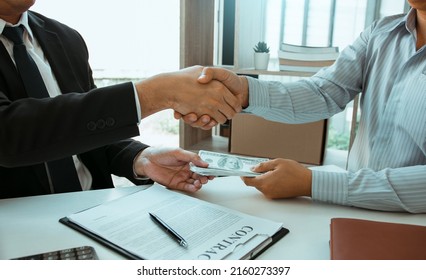 Two corporate businessmen shaking hands while one man places money on document in office room with corruption concept. - Shutterstock ID 2160273397