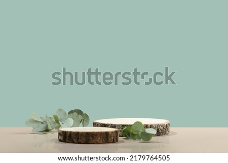 Two cosmetic product podiums mockup. Background for presentation of cosmetic. Minimal modern product display on neutral blue background. Wood slice podium and green leaves. Concept scene