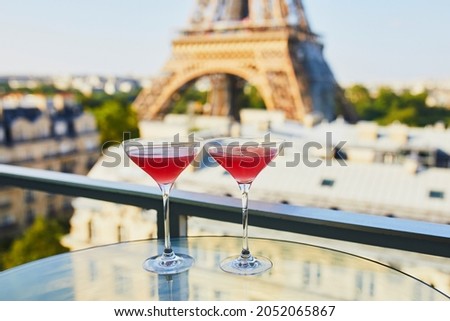 Two Cosmopolitan cocktails in traditional martini glasses on a glass table with view to the Eiffel tower, Paris, France