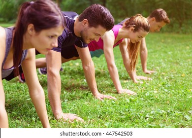 Two couples doing crossfit exercises performing push-ups in the planking position on green grass outdoors in a park - Powered by Shutterstock