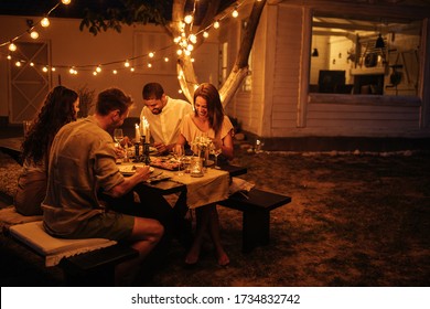 Two Couples Enjoying Dinner In A Backyard