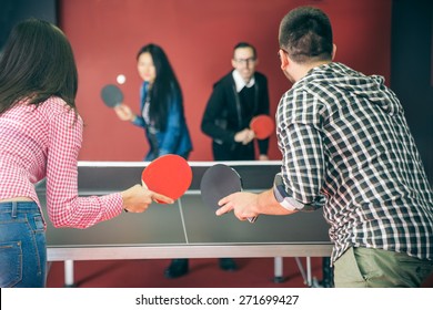 Two couples of young people playing ping pong in a hostel - Four students with ping pong paddles having fun in a pub