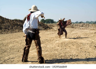 Two Cowboy Outfit Costume With A Gun Held In The Hand On Gun Fight Against Sun Light On The Bottle Field.