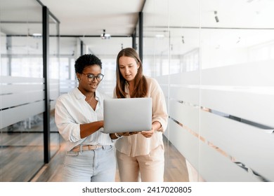 Two coworkers chatting during coffee break standing in glass hall of office building. African-american female employee explain something to colleague, sharing ideas - Powered by Shutterstock